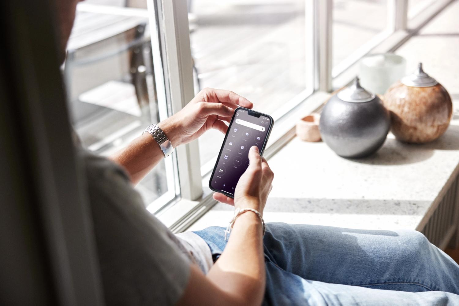 Mann som sitter i en vinduskarm og ser på en mobiltelefon.