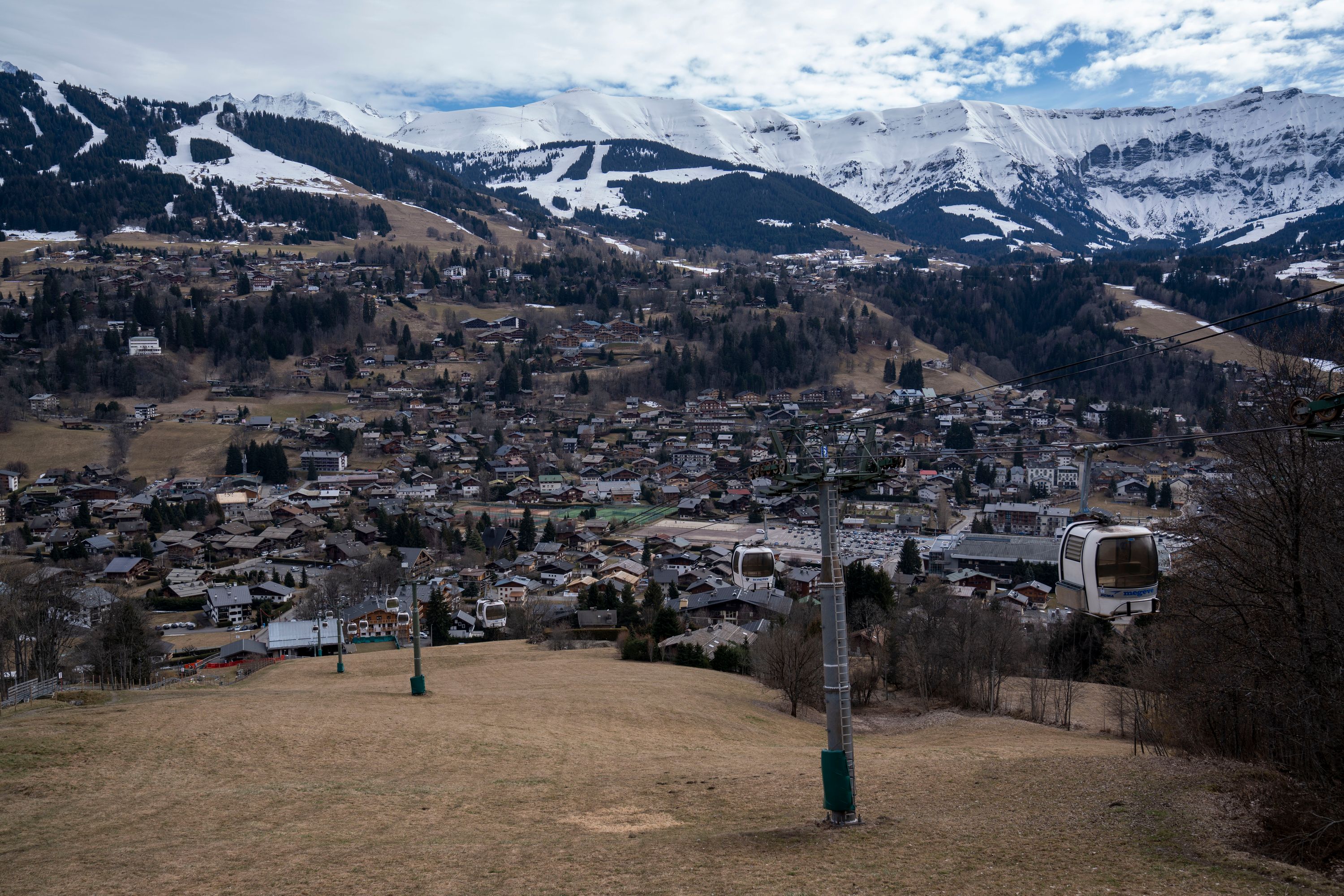 Alpelandsby uten snø med snødekte fjell i bakgrunnen