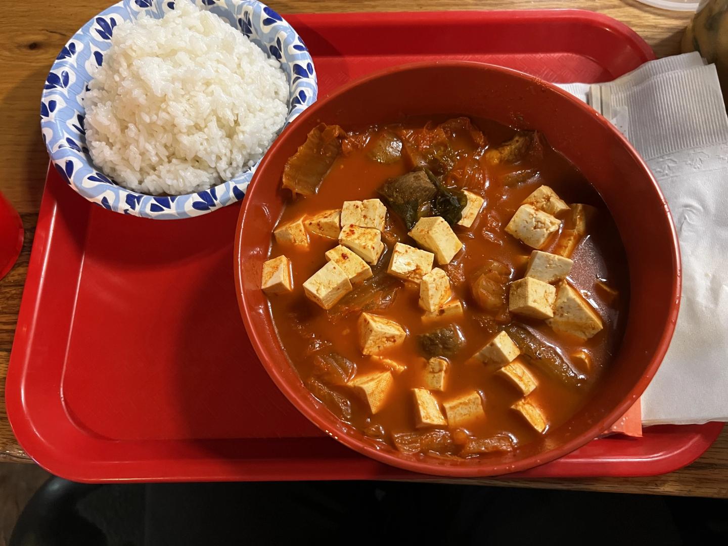 kimchi jjigae with a side of white rice on a red cafeteria tray