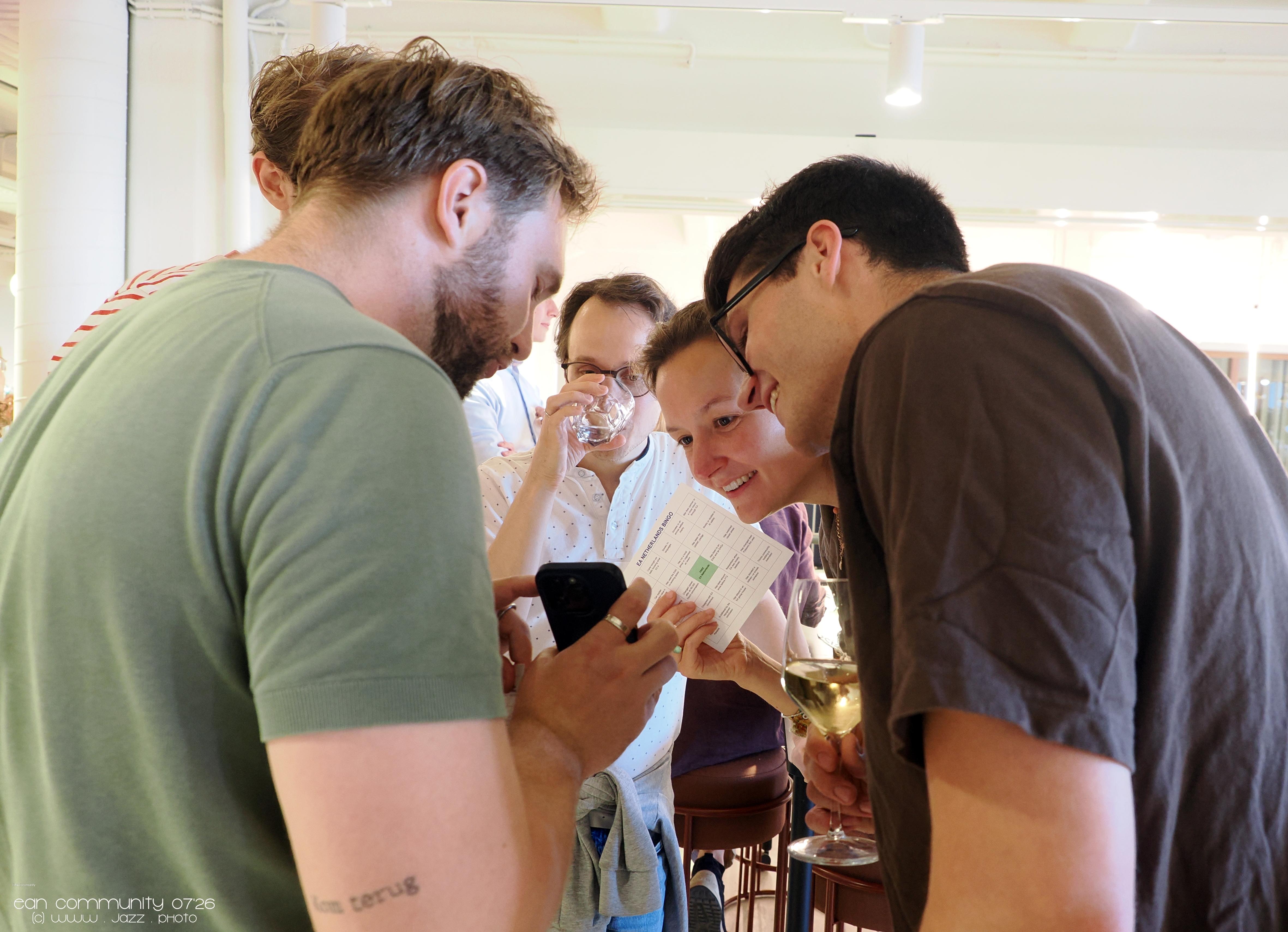 A group of smiling people gathered around a smartphone screen, with one person holding a small card.