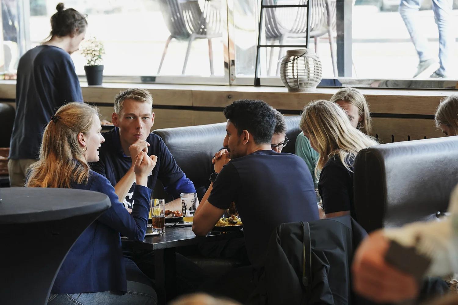 Een foto van een groepje effectief altruïsten aan en tafeltje met drankjes. Eén persoon kijkt serieus richting de camera.  