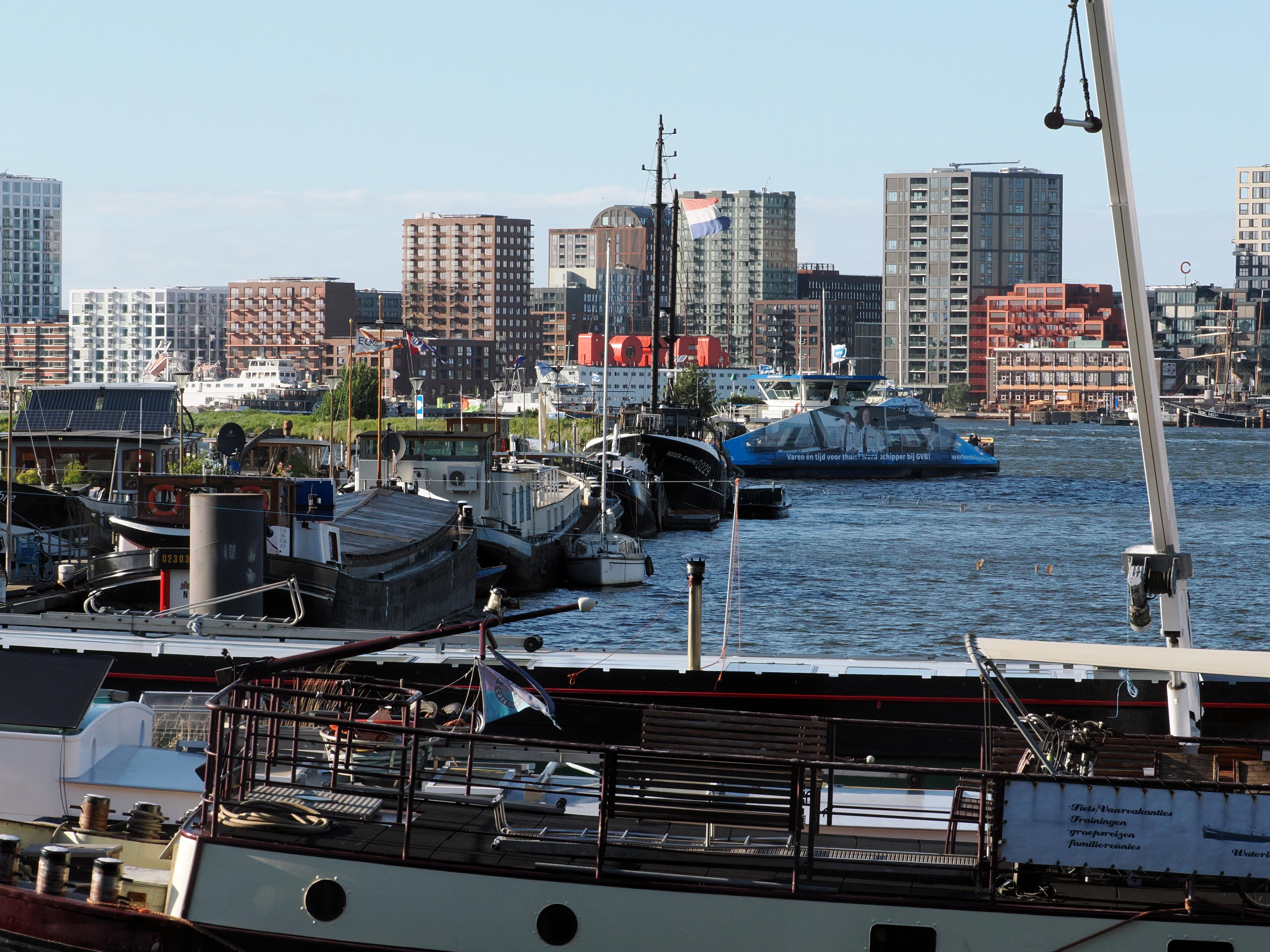 View of a city waterfront with docked boats, a blue ferry, and a modern skyline.