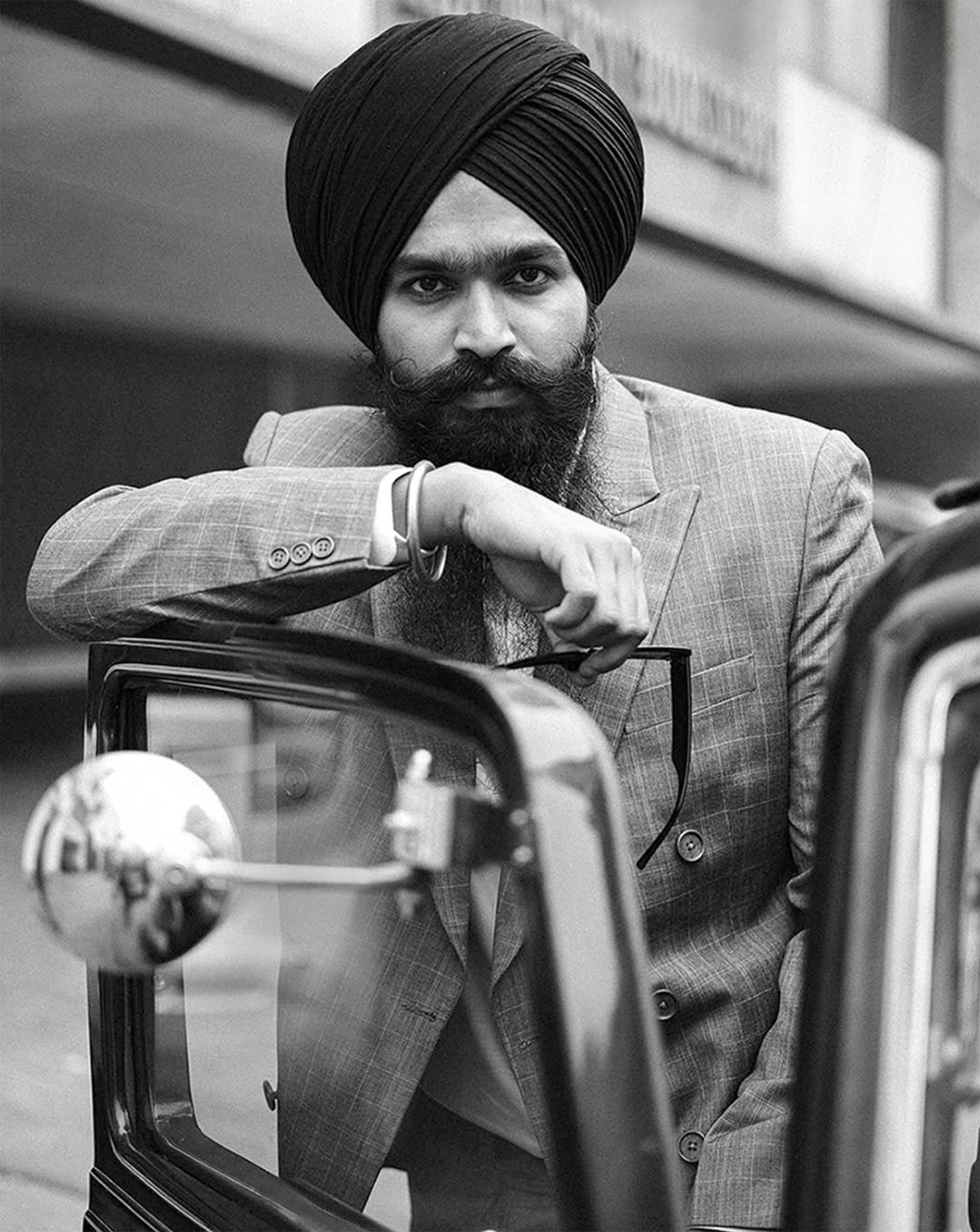 Maninder Singh of House of Singh in a black and white editorial portrait beside a classic car.