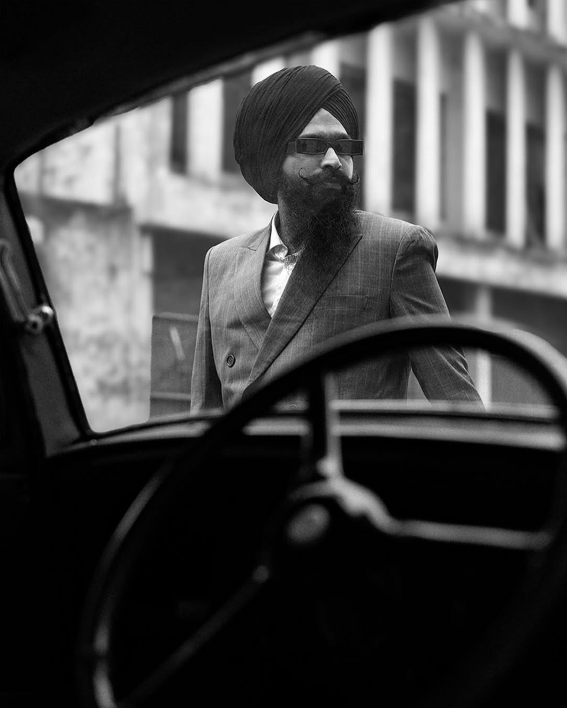 Maninder Singh of House of Singh in a black and white editorial portrait beside a classic car.