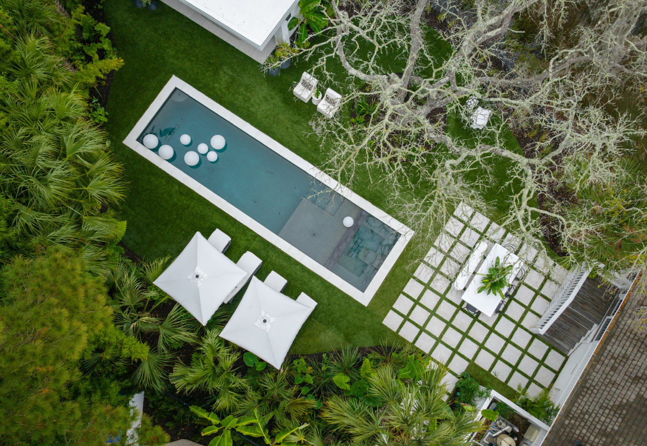 an aerial view of this Tilly client's inviting completely transformed outdoor oasis with lots of green, a paver walkway, stone, pergola and a pool house