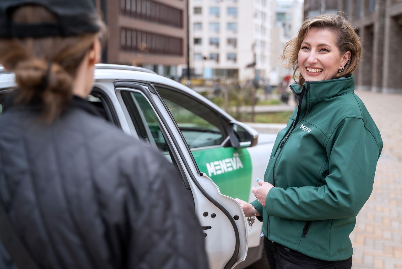 Vihreätakkinen Menevä-host avaa auton oven asiakkaalle
