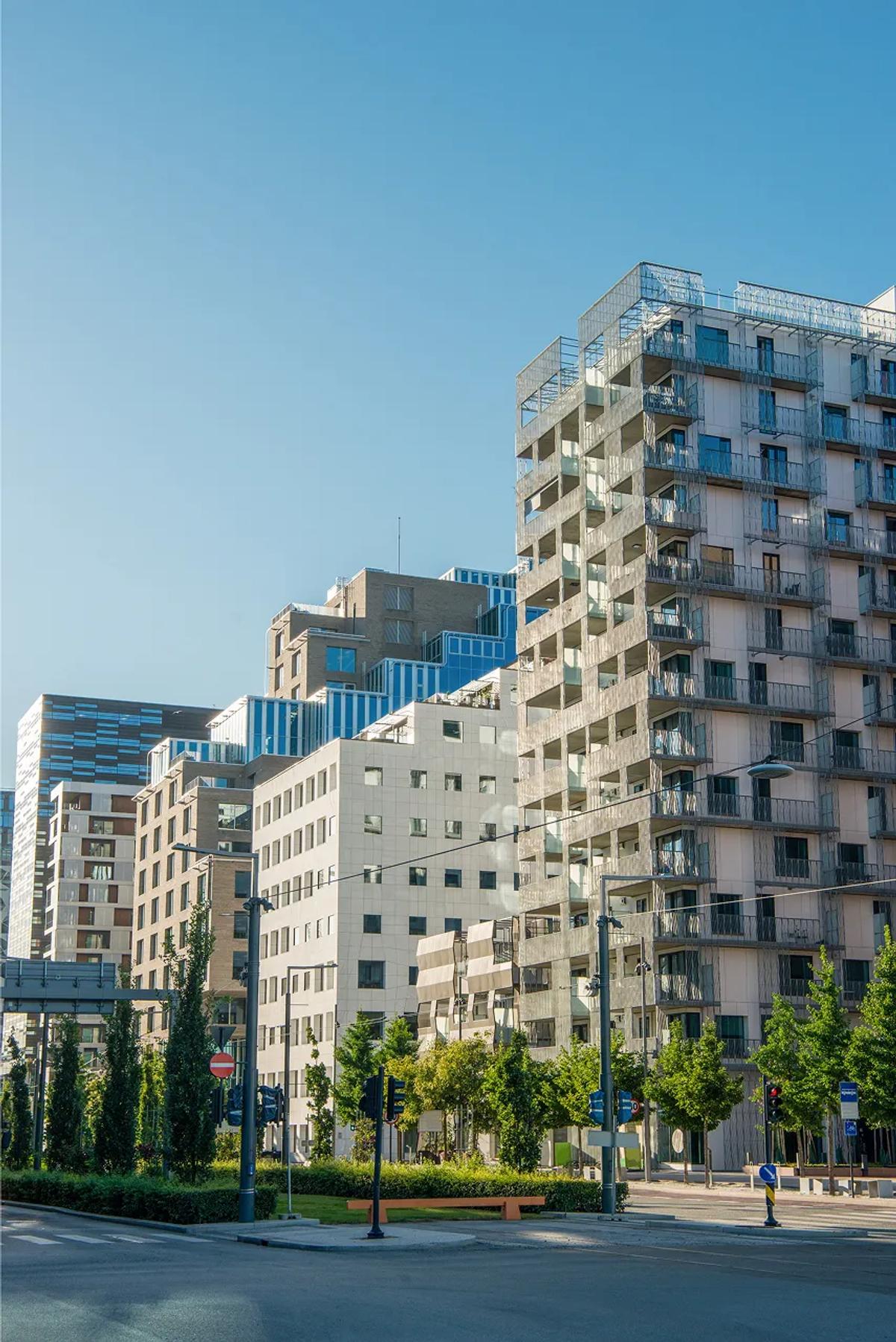 Moderne boligblokker med balkonger ved en bygate under en klar blå himmel.