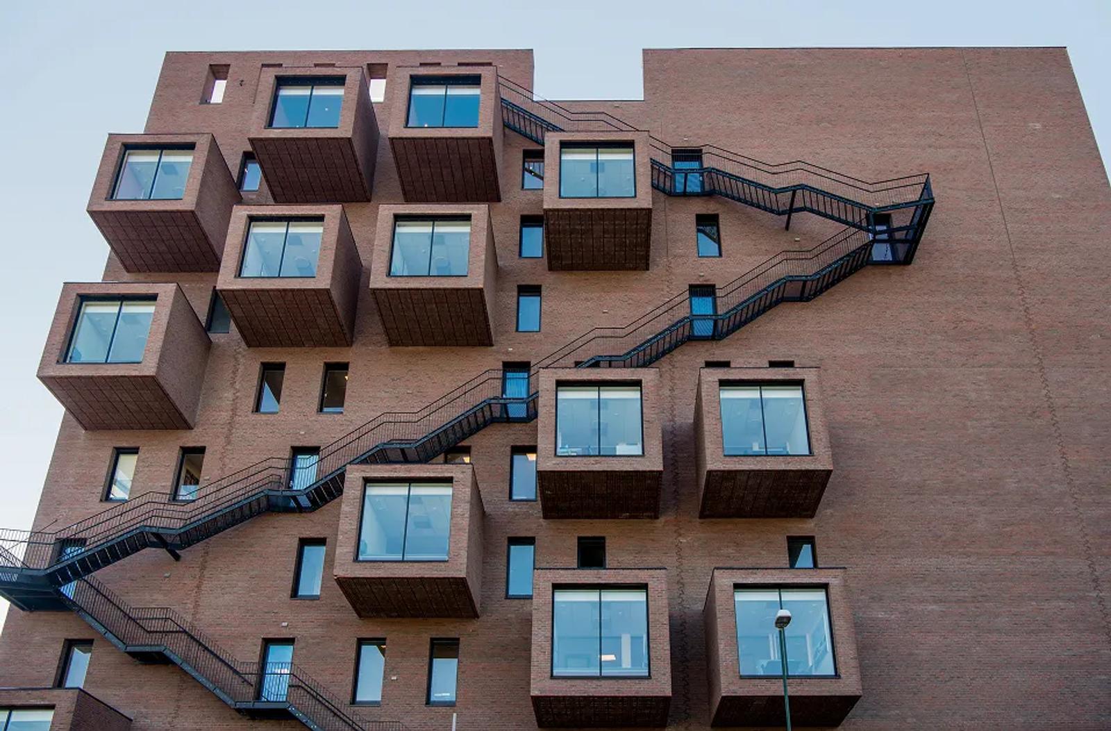 Moderne murbygning med fremspringende firkantede glassvinduer og utvendig svart trappelinje.