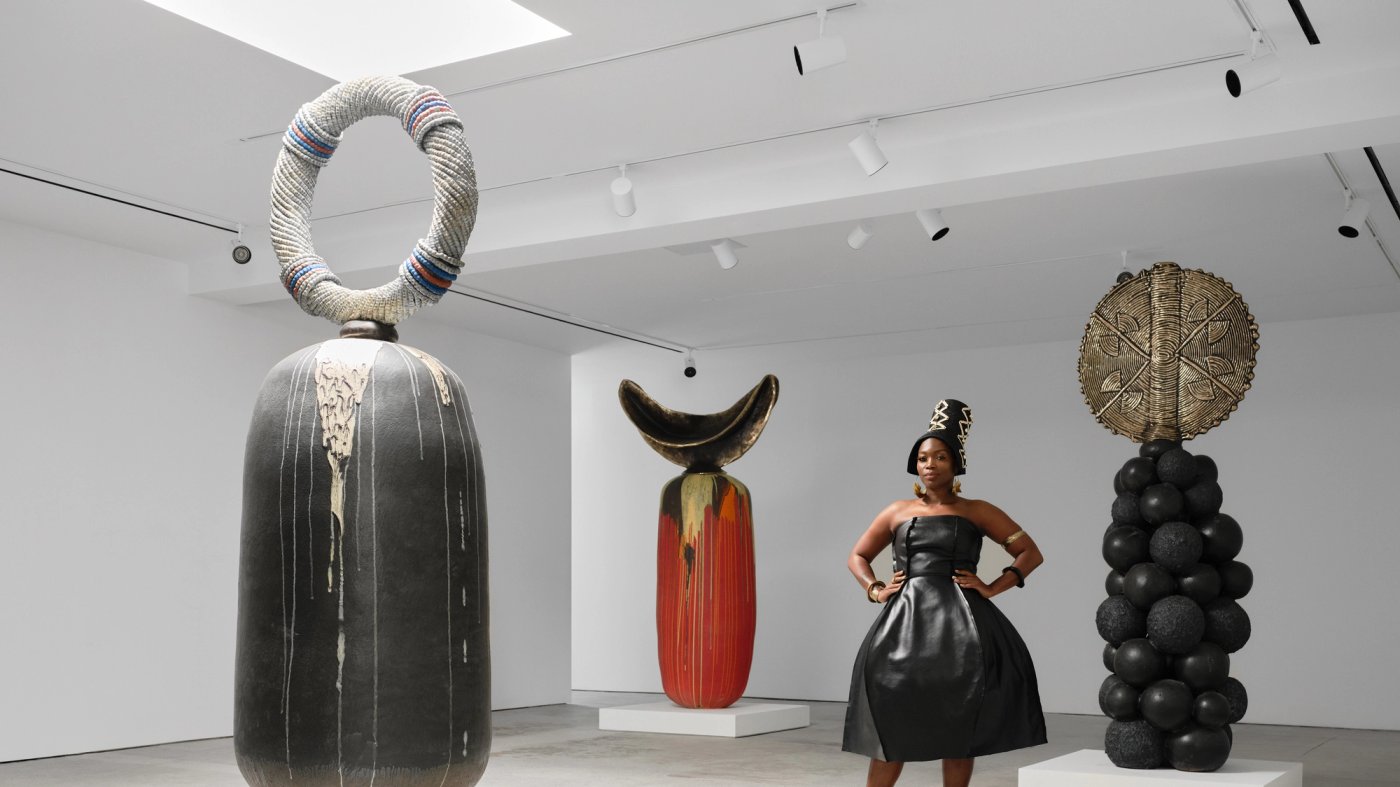 Zizipho Poswa standing in a gallery among large sculptural vessels with elaborate curved and beaded forms