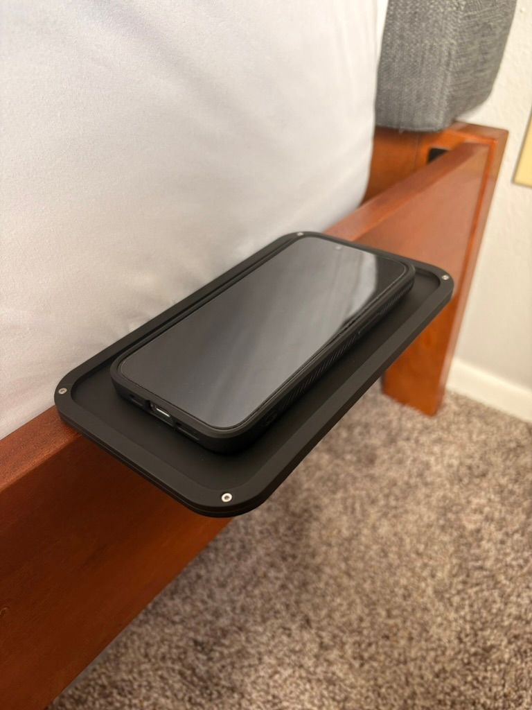 Black modular bed shelf holding a phone