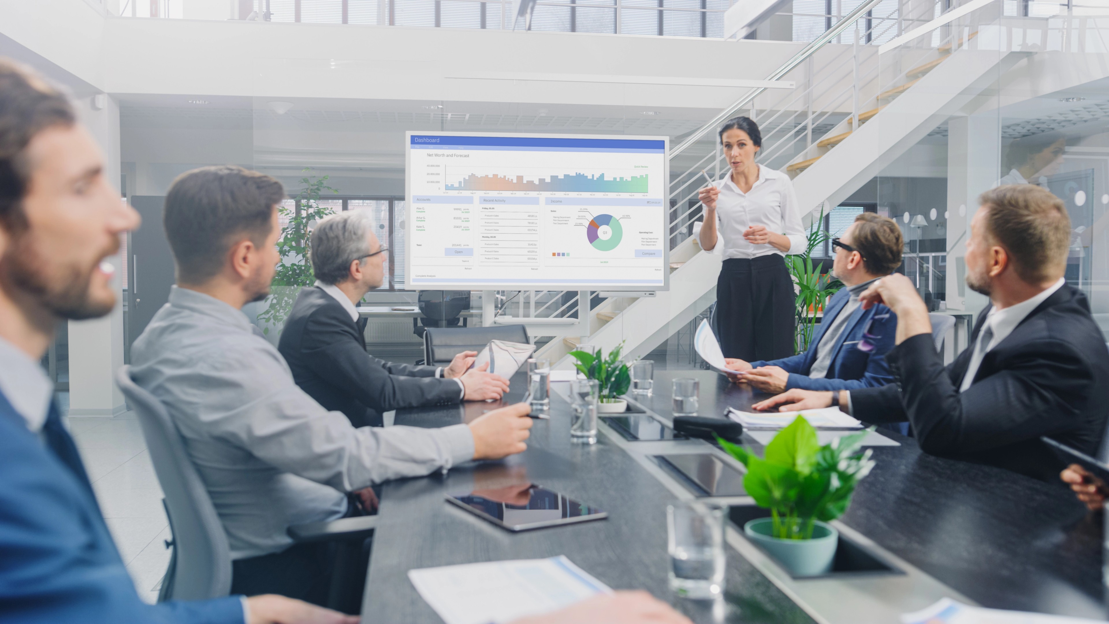 Female analyst describing data on a screen to a group of board members