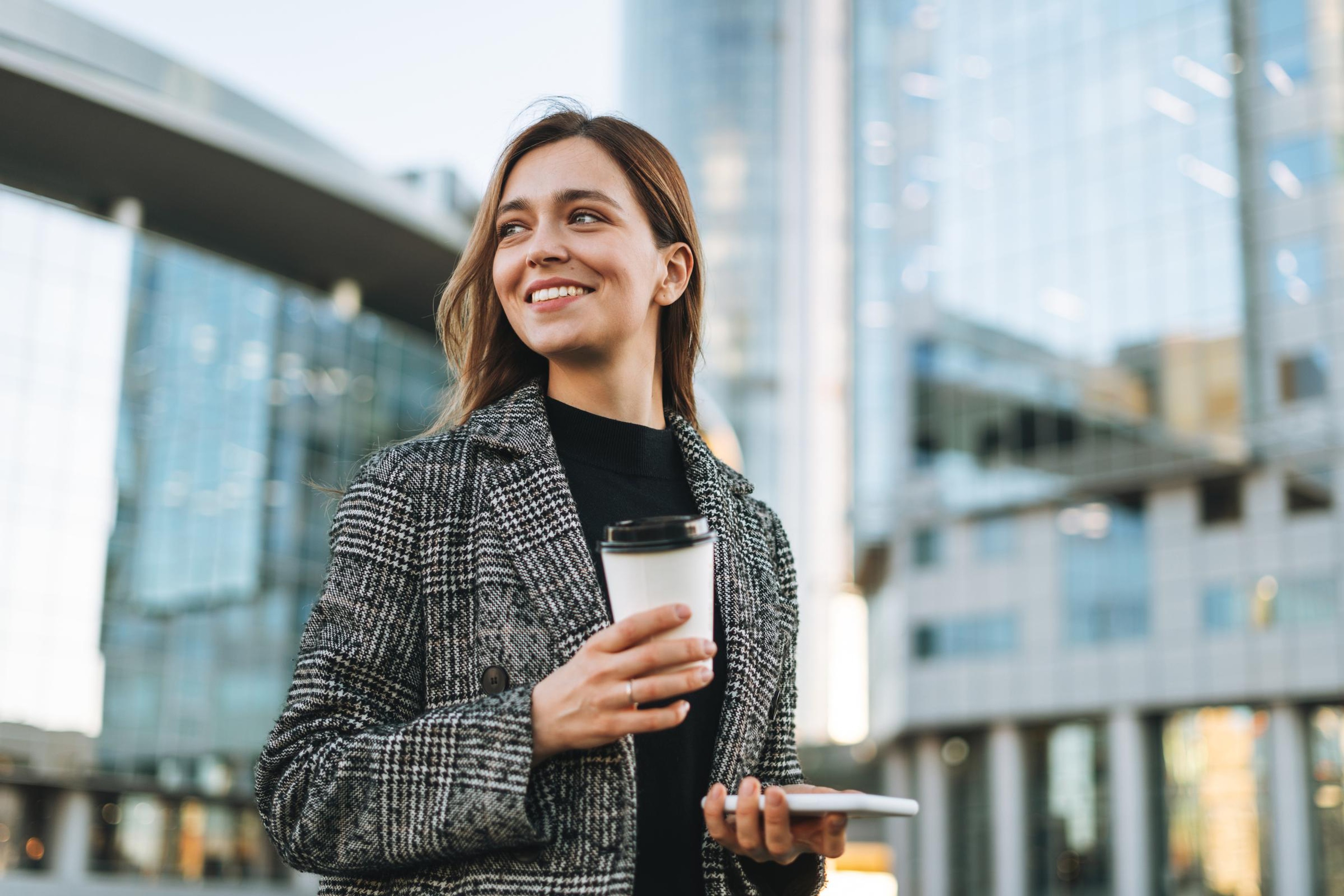 Woman uses phone in one hand as she walks down the city street on her way to a meeting to discuss how the cloud controls framework is streamlining certifications for her company