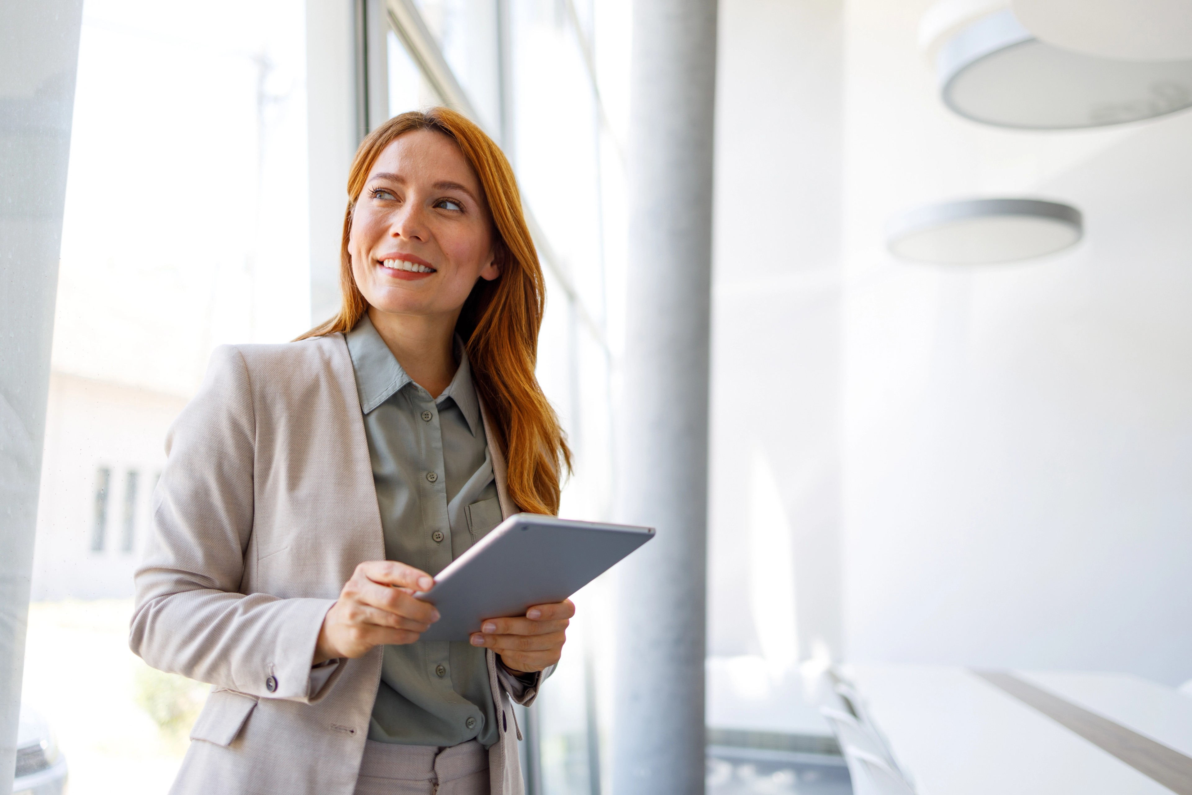 Confident businesswoman smiling, holding a digital tablet in a contemporary office