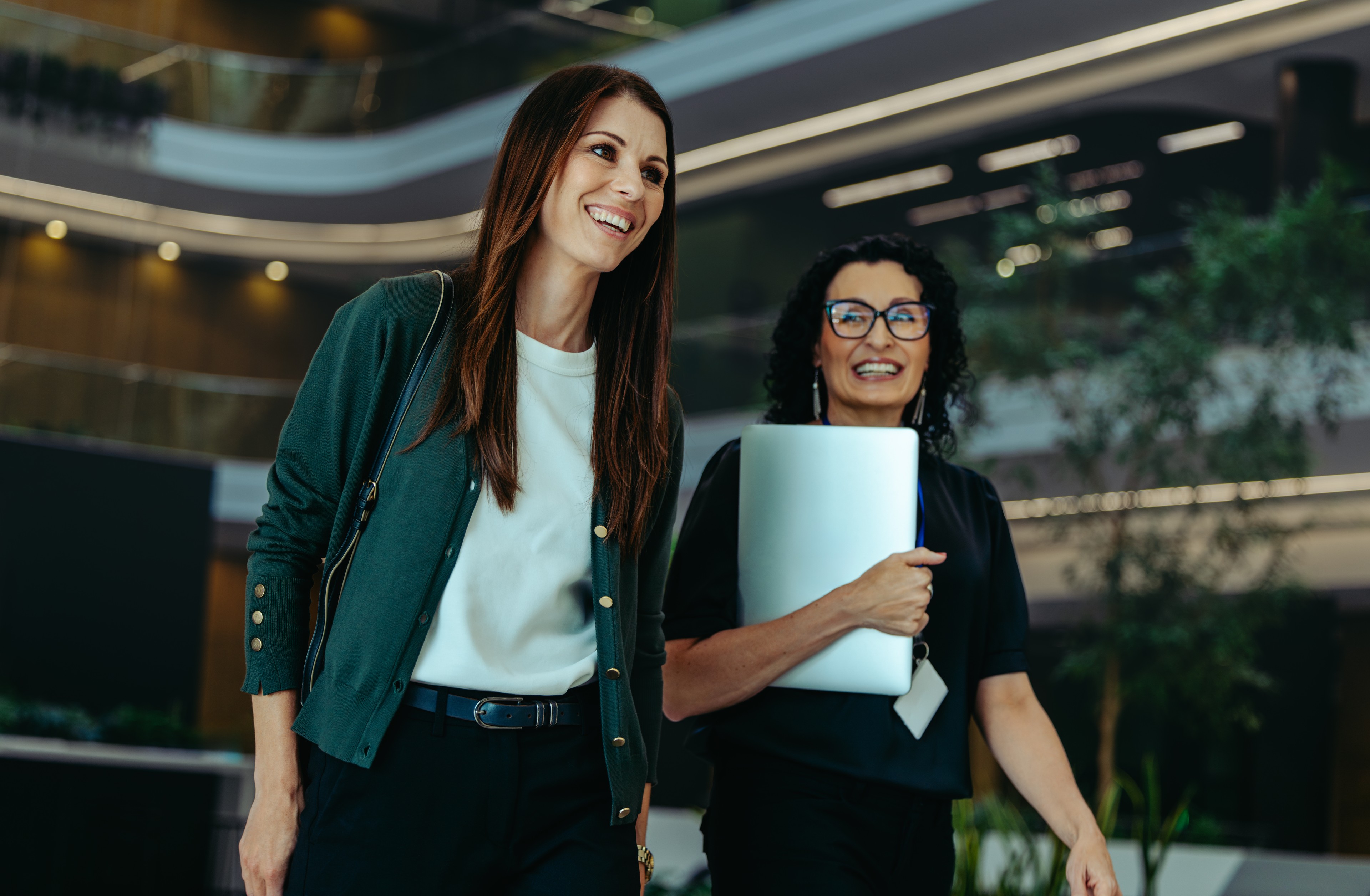 Two female professionals in a corporate setting, walking through a modern building.