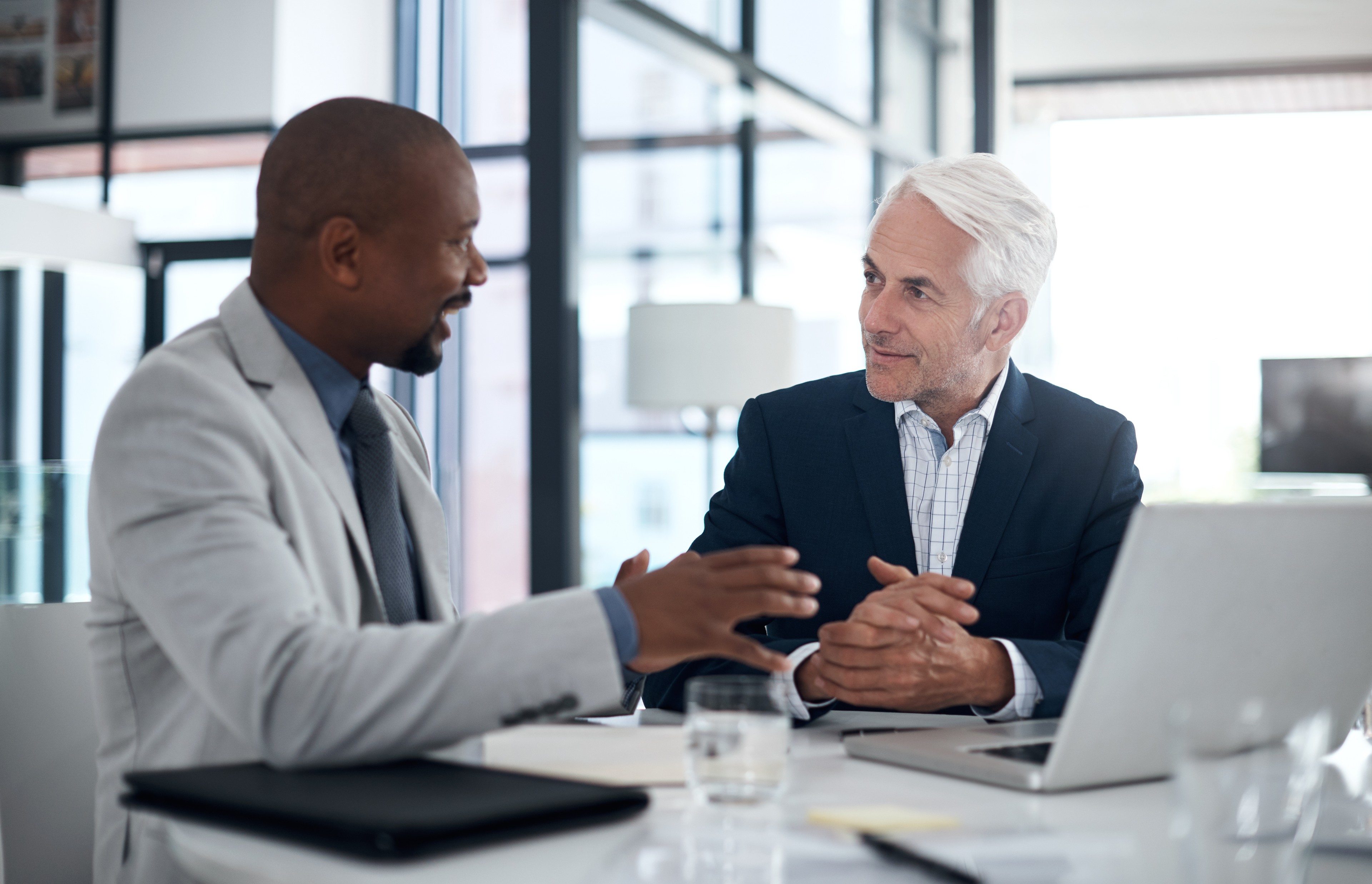 Two businessmen talking over a laptop display.