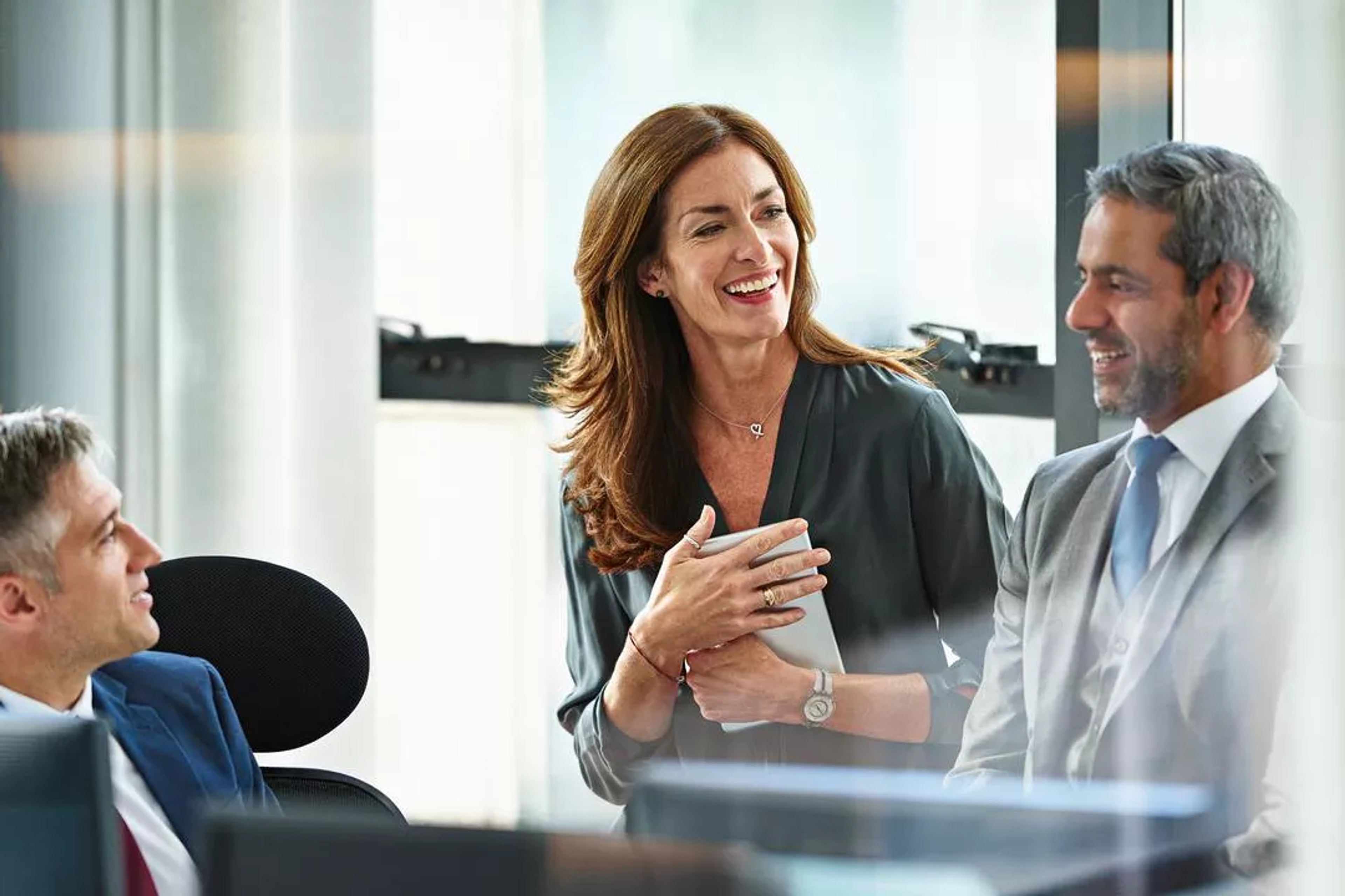 Three people stand in an office discussing how to prepare for a board presentation