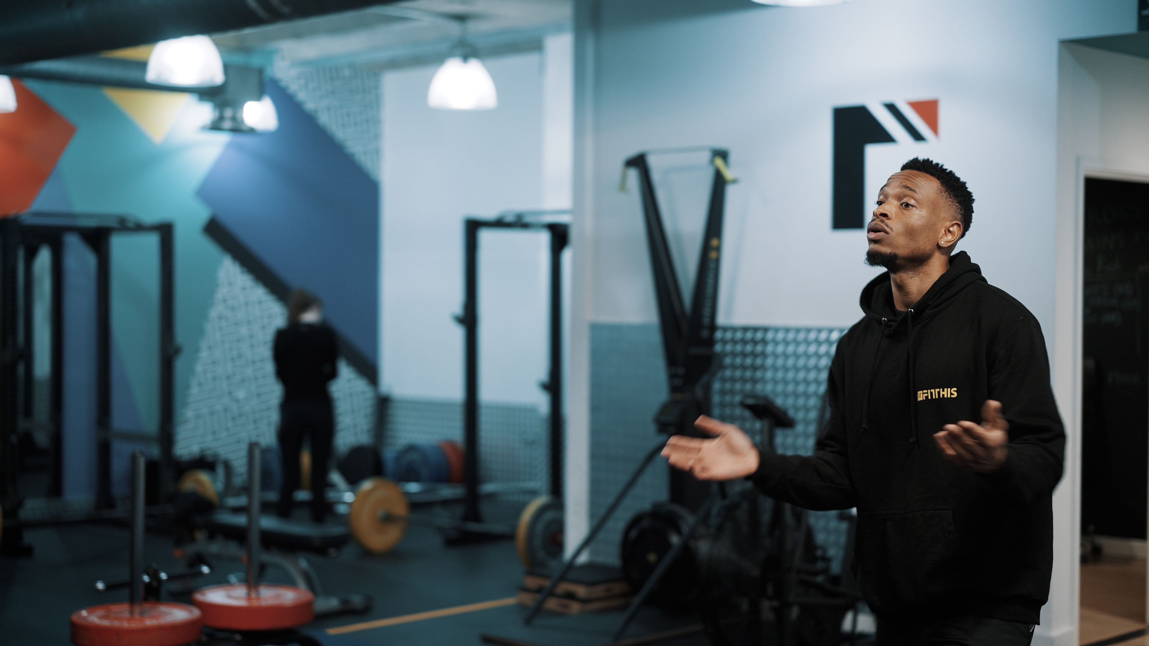 A trainer on the gym floor at Fit This, with the squat racks behind