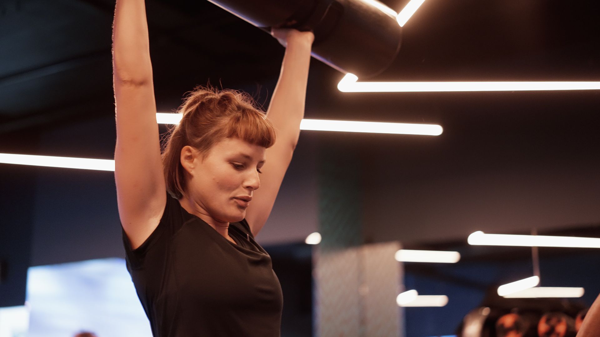 A member pressing a barbell overhead in the studio at Fit This