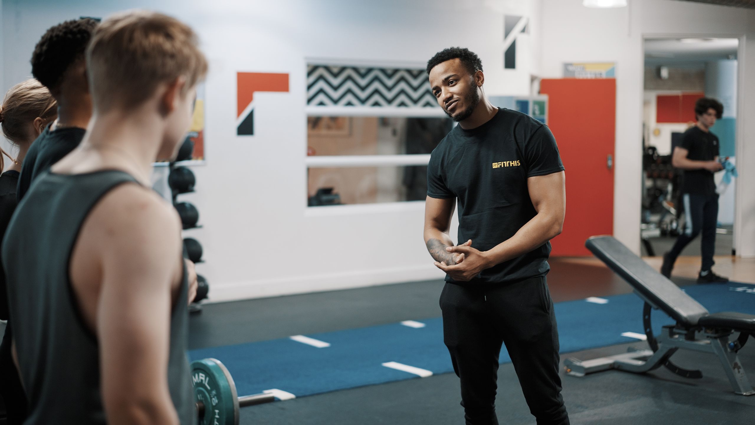 A trainer talking two members through a session on the gym floor