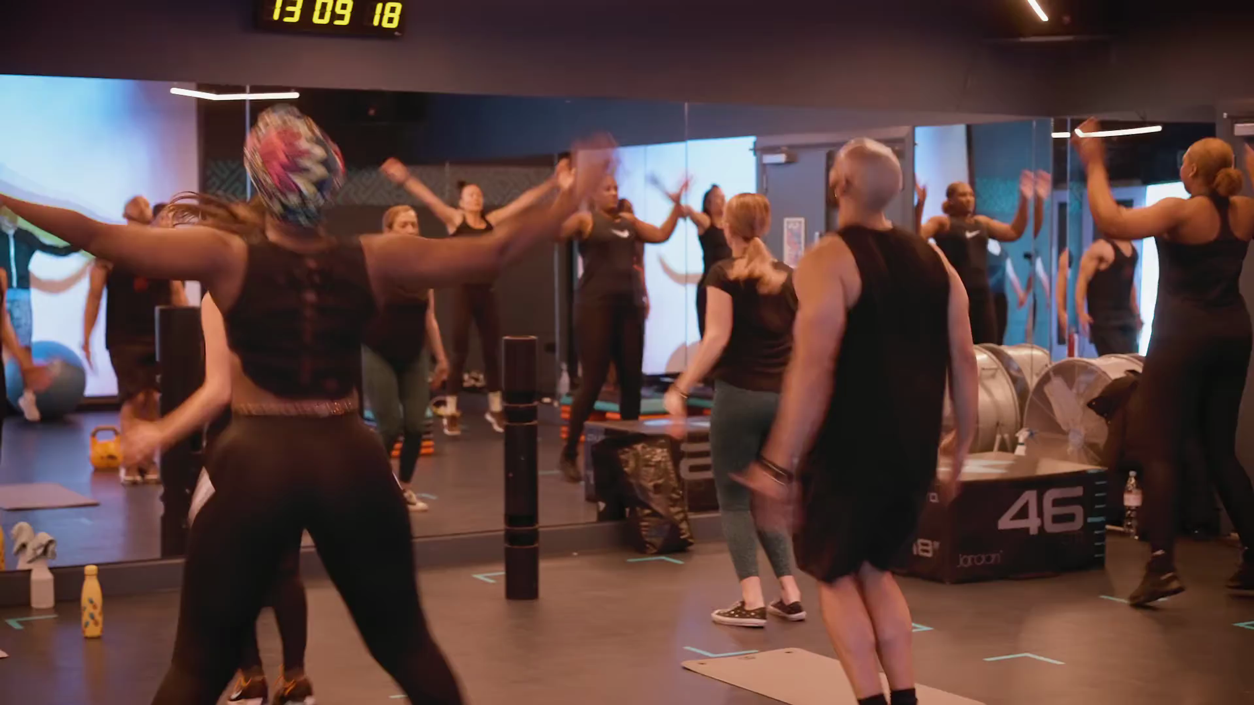 Members reaching overhead together in a busy studio class at Fit This