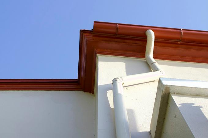 Looking up at a red gutter and fascia on the corner of a rendered house with a cream downpipe.