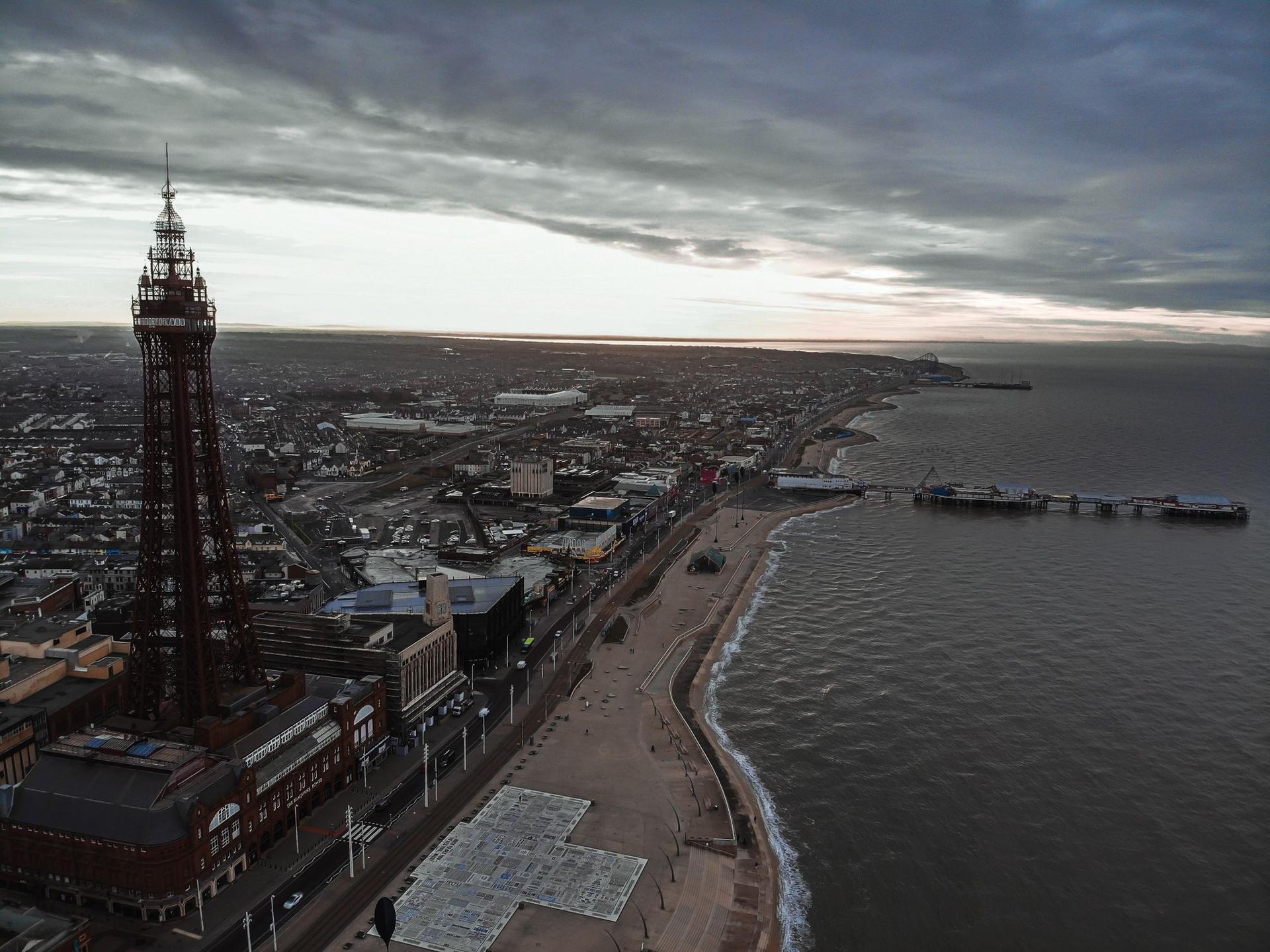 An aerial view of Blackpool Tower, the promenade and Central Pier under a moody grey sky.