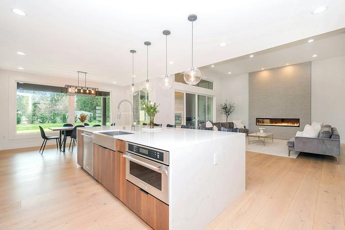 A bright open-plan kitchen and living area with a large island, pendant lights and a linear fireplace.