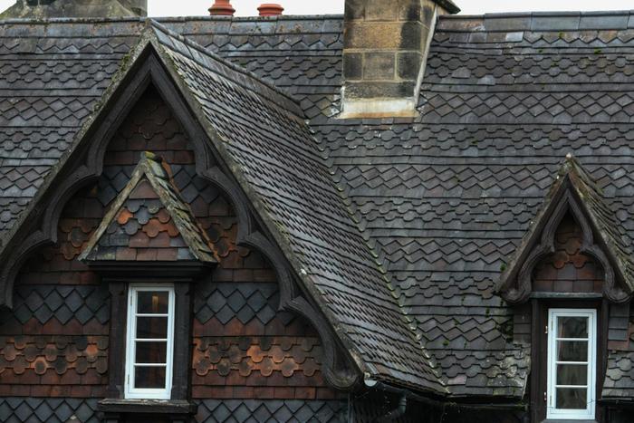 A steep slate roof with a stone chimney and two ornate gabled dormer windows.