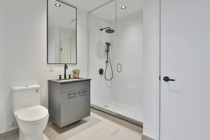 A compact modern bathroom with a walk-in shower, a grey vanity unit and a black-framed mirror.