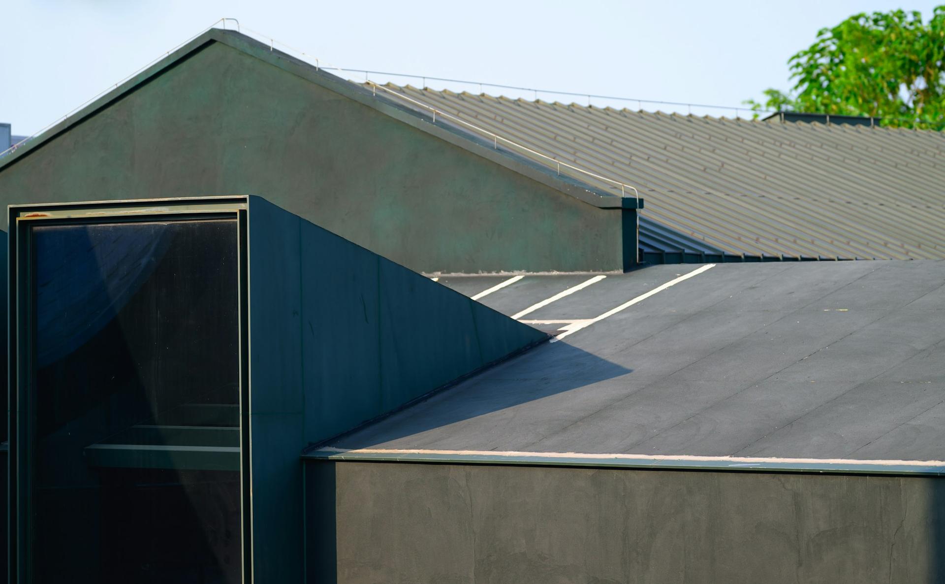 A dark membrane-covered flat roof meeting a rendered wall, with a pitched metal roof behind.