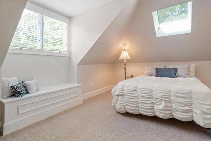 A loft bedroom with sloping ceilings, a skylight, a window seat and a double bed.