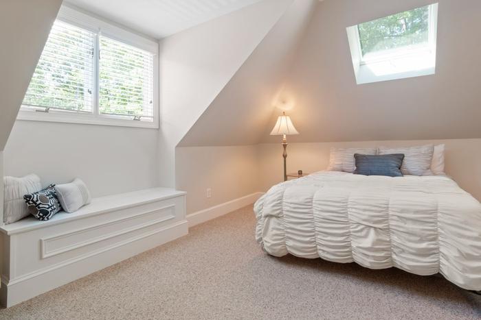 A loft bedroom with sloping ceilings, a skylight, a window seat and a double bed.