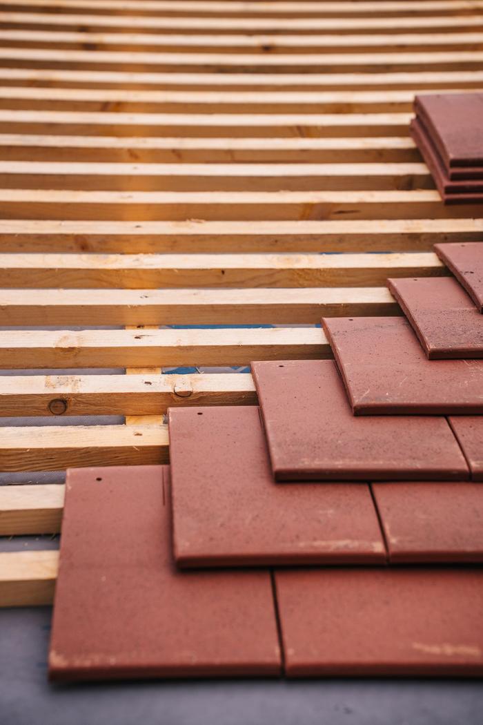 A close-up of red clay plain tiles being laid over timber roof battens.