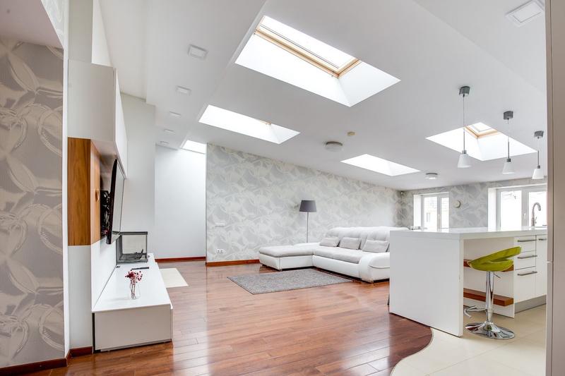 A bright converted loft living space with several roof windows, a white sofa and a breakfast bar.
