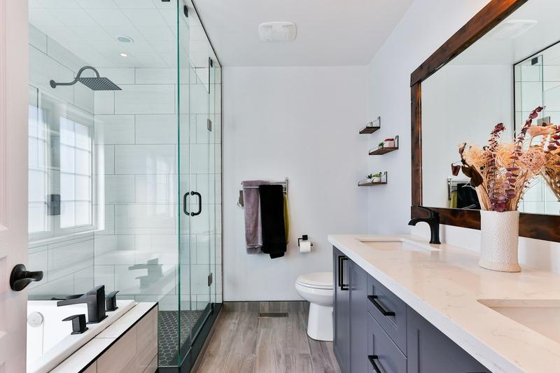 A modern bathroom with a glass shower enclosure, a double vanity and a large wood-framed mirror.