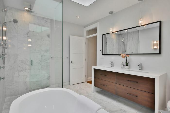 A renovated bathroom with marble tiles, a glass shower, a freestanding bath and a double vanity.