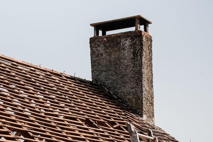 A weathered rendered chimney stack beside a pitched roof stripped back to its battens.