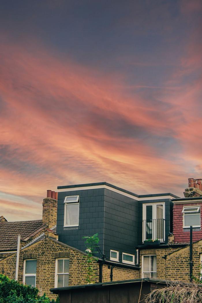 A modern rear dormer loft conversion on a yellow brick terrace under a pink sunset sky.
