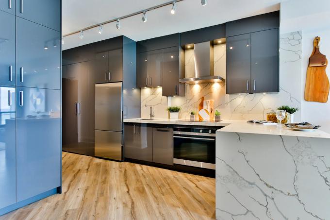 A modern kitchen with glossy grey cabinets, a marble waterfall worktop and splashback, and wood-effect flooring.