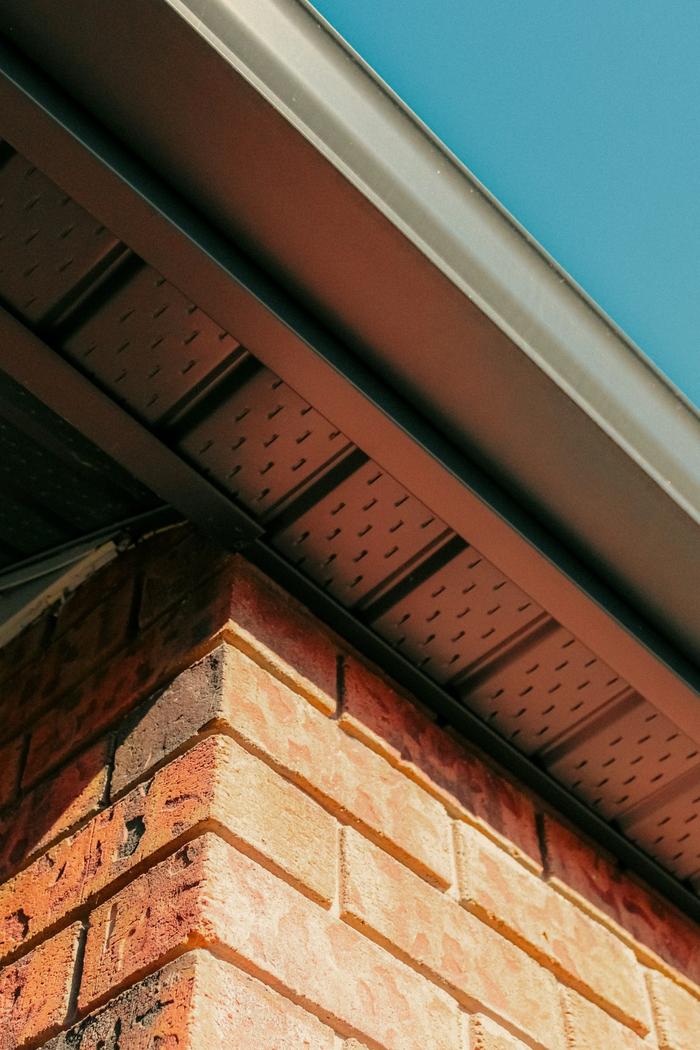 A close-up of a new gutter, fascia and vented soffit above a red brick wall.