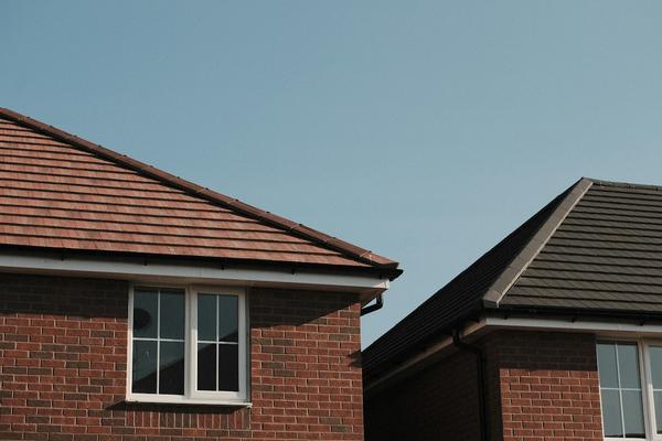 The new tiled roofs, white fascias and black gutters of two red brick houses against a clear blue sky.