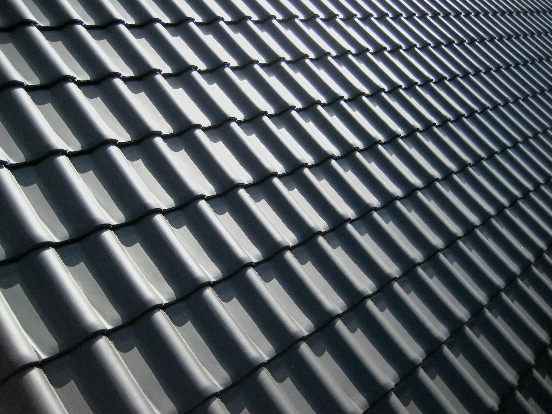 A close-up pattern of dark grey interlocking roof tiles casting sharp shadows in bright sunlight.