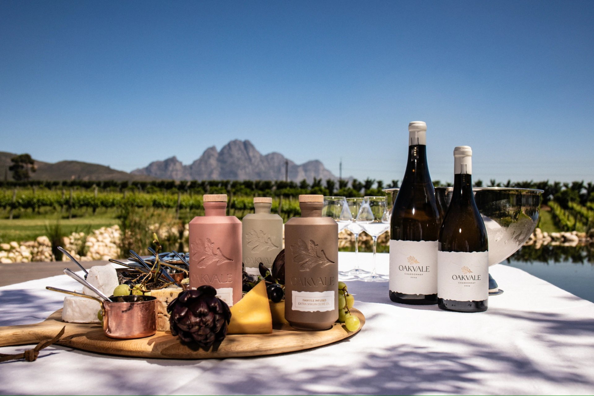 Oakvale olive oils and Chardonnay displayed with food in front of the vineyard and mountains