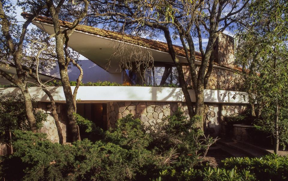 Casa con terraza volada entre árboles y muros de piedra
