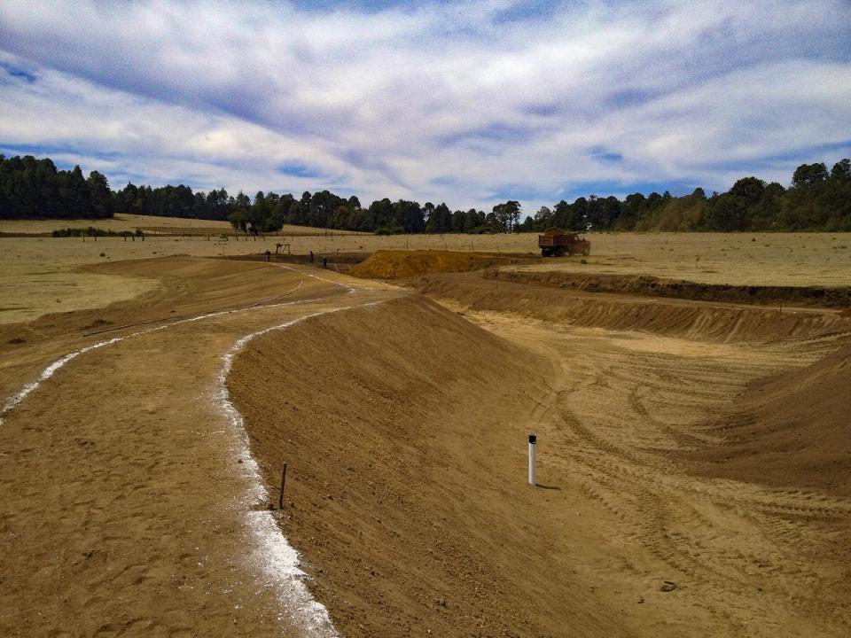 Talud de tierra en curva con trazo blanco y cielo nublado