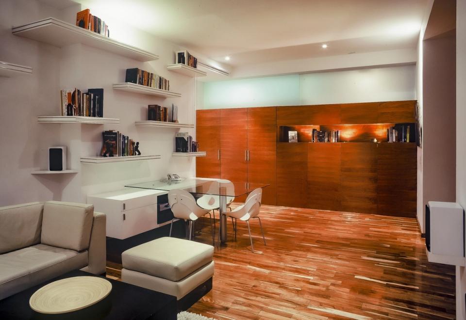 Estudio con repisas flotantes, escritorio de cristal y muro de madera