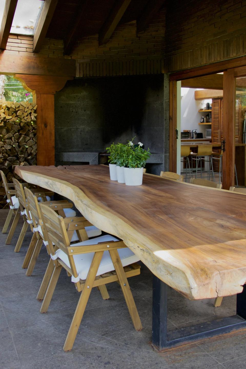 Mesa larga de madera en la terraza techada con chimenea de piedra al fondo