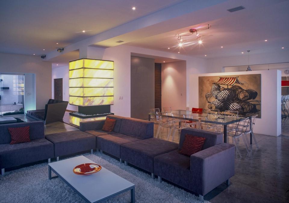 Estancia con sala gris, chimenea iluminada y comedor de cristal al fondo