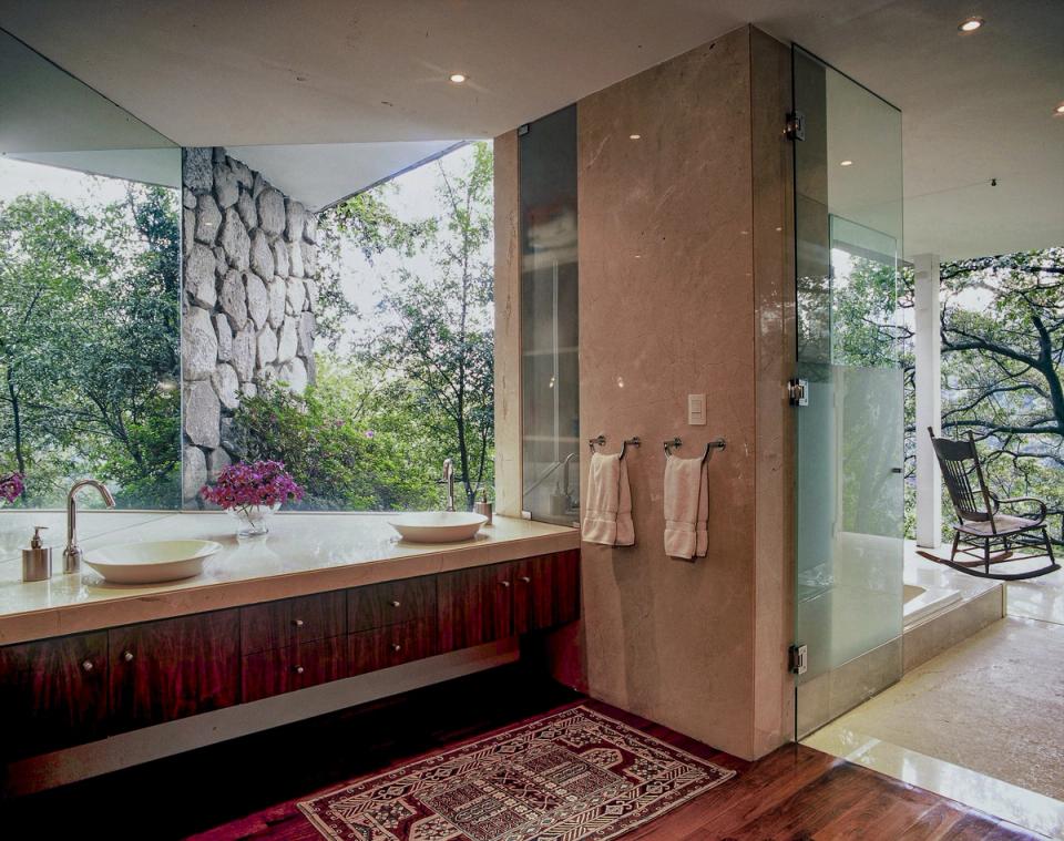 Baño con muro de piedra y ventanal hacia la vegetación