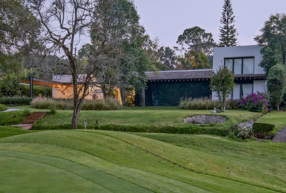 Casa entre árboles con techo de teja y volumen blanco al atardecer